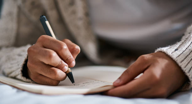 Cropped shot of a man writing in a notebook on his bed at home