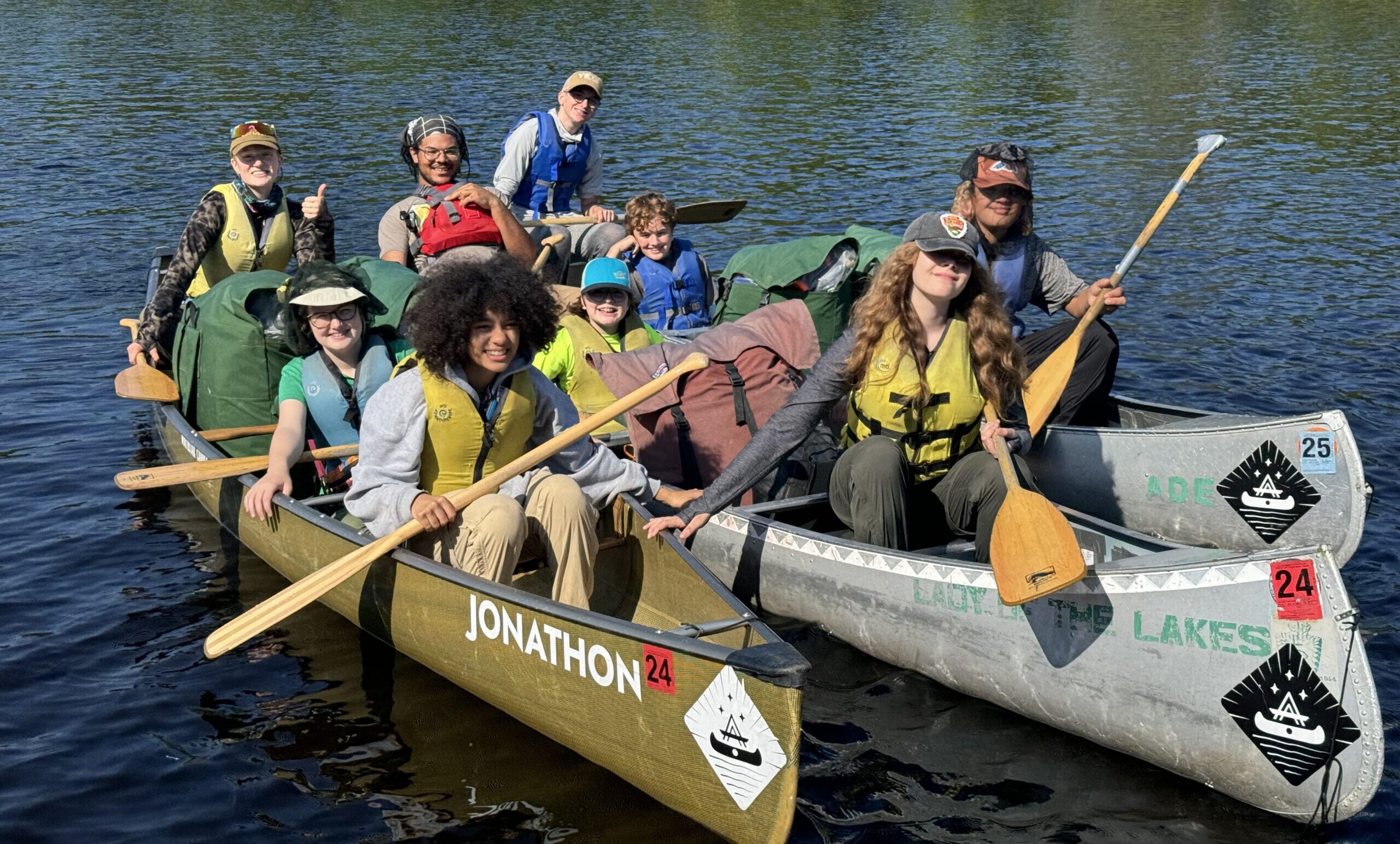 A group of students smiling at camera across three canoes in BWCA.