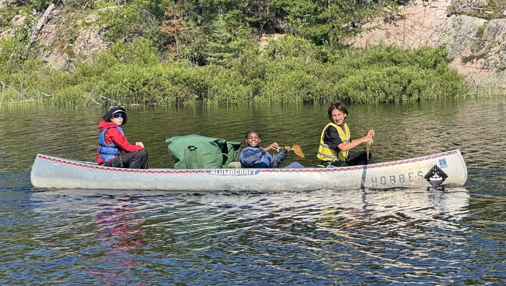 Three students paddling in a canoe.