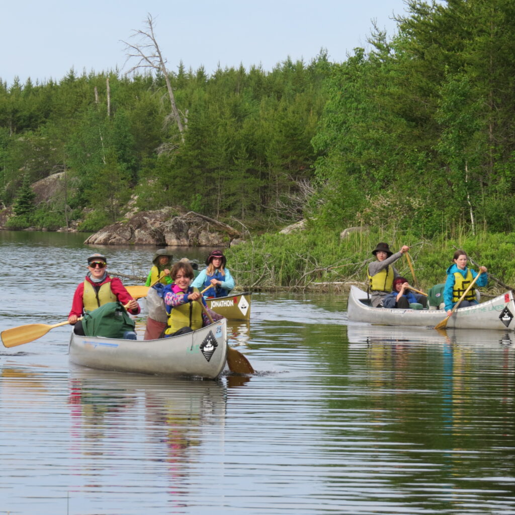 Multiple canoes of students paddling.