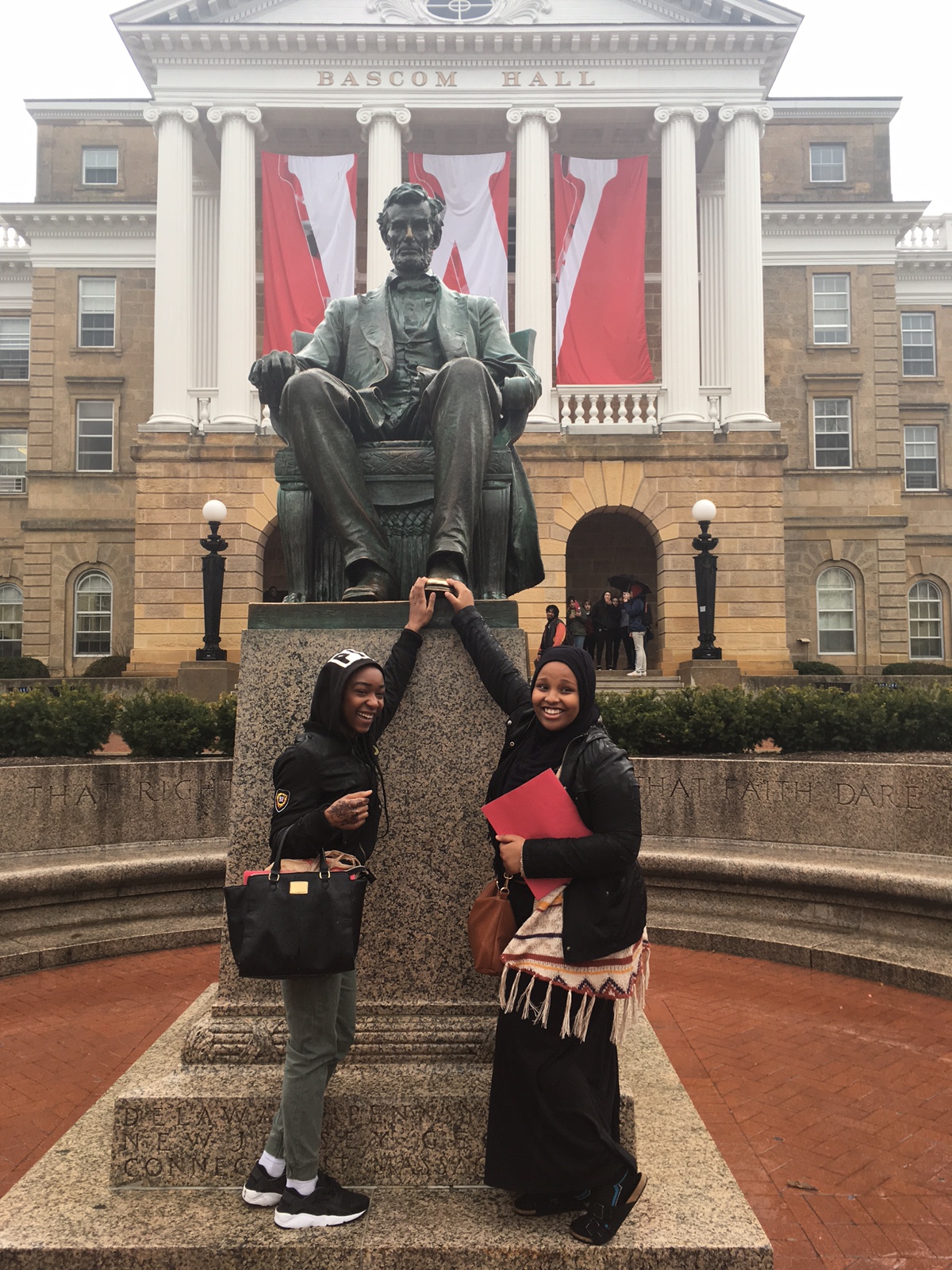 Two PS students touch a statue of Abe Lincoln infront of the University of Wisconsin - Madison logo